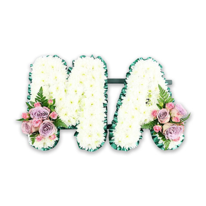 The image shows an elegant funeral letter tribute spelling out the word "MA," designed with the care and precision you would expect from an experienced local florist serving Woodside families. Both letters are bold and easy to read, cut in a classic block style and then completely covered in crisp white chrysanthemums. The blooms are densely packed, forming a thick, almost quilted layer that gives the letters a soft, cloud-like presence. Each chrysanthemum head appears fresh and full, the tidy ring of petals creating a calm, ordered texture that feels soothing at a time of loss. Along the outer edge of each letter, a deep emerald green ribbon has been neatly gathered and pleated, creating a ruffled frame. This rich green outline not only defines the contours of the M and the A but also balances the whiteness with a subtle, natural contrast, much like the mix of stone and greenery you might notice walking past Woodside's older churches and memorial gardens. At the base of the left vertical of the M and the right leg of the A, two carefully matched flower groupings add a soft blush of colour. Here, blush pink roses, lilac roses, and smaller pink spray roses are tucked together, their velvety petals spiralling inward and outward in different stages of bloom. Light, airy fern fronds and sprigs of foliage peek between the roses, bringing movement and a hint of woodland freshness to the design. Set against a plain, bright backdrop, the focus rests entirely on the tribute's structure and sentiment: a personalised floral "MA" that speaks of a cherished mum, mama, or maternal figure whose memory is lovingly honoured through pure white flowers, gentle pastel tones, and thoughtful craftsmanship.