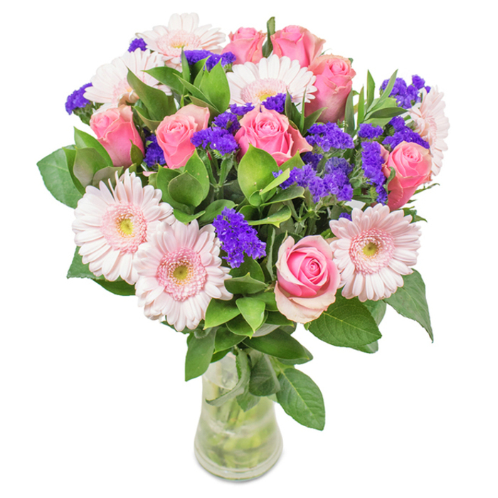 An elegantly curated bouquet presented in a transparent glass vase, highlighted by the serene backdrop of Woodside's peaceful ambiance. Centrally, you'll notice a harmonious gathering of seven to nine roses in shades from pastel blush to medium pink, some tightly closed, others unfolding into exquisite spirals. These are complemented by about five to seven pale pink gerbera daisies, their generous round faces and delicate, radiating petals brightening the arrangement, each disk glowing with a soft, near-ivory center. Interlaced throughout the bouquet, vibrant purple statice lend both colour and texture-their clusters reminiscent of fresh blossoms found in Woodside's parks. Lush green foliage cradles the blooms, imparting an invigorating scent and visual abundance. The clear vase reveals the neat alignment of stems and shimmering water inside, underscoring the arrangement's freshness and everyday elegance. This locally inspired floral display-crafted for birthdays, anniversaries, or thoughtful gifting-captures Woodside's gentle community flair and the heartfelt joy of expertly arranged flowers.